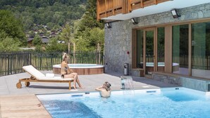 A swimming pool with lounge chairs and a hot tub, surrounded by a stone wall and wooden deck. - Wifi, swimming pool, terrace, balcony, tv, ski locker, 43-61m², Samoëns (Samoëns)