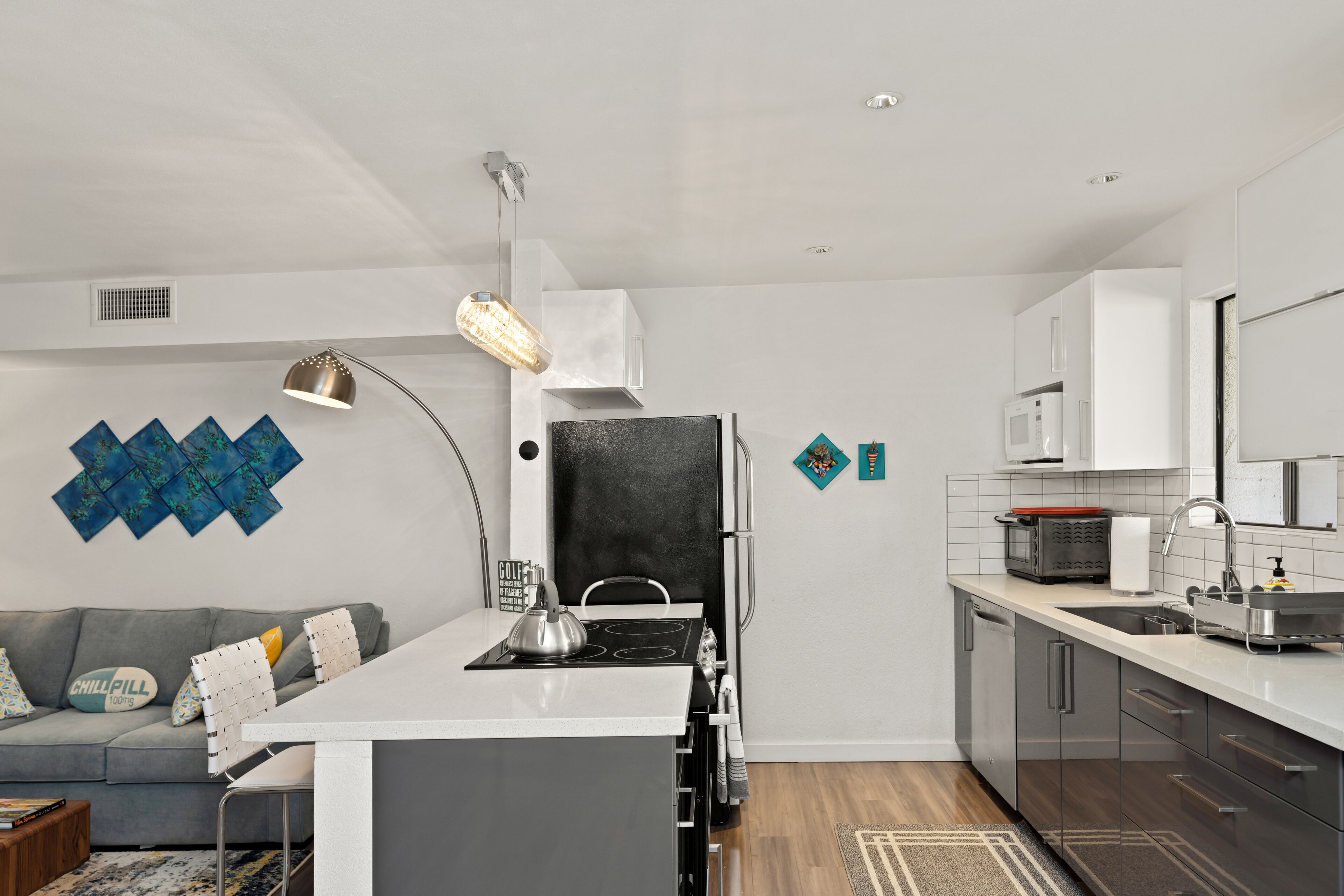Een moderne keuken met een centraal eiland, witte kastjes en een grijze bank met decoratieve kussens.
