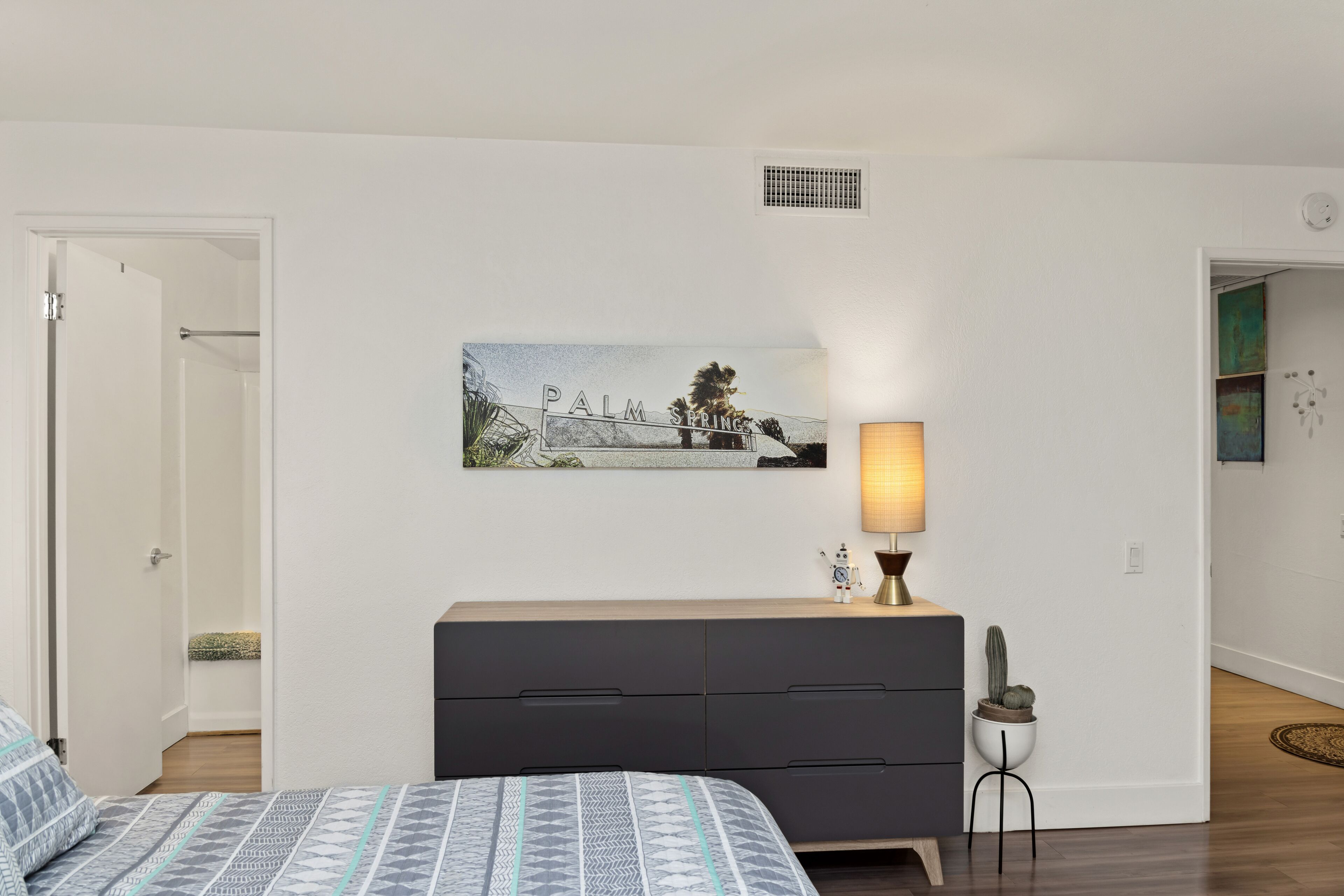 A bedroom with a bed, a dresser, a lamp, and a painting on the wall.