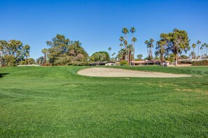 A golf course with a well-maintained green, sand bunkers, and a clear sky.