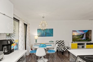 A modern kitchen with a coffee maker, a dining table with blue chairs, and a TV on the wall.