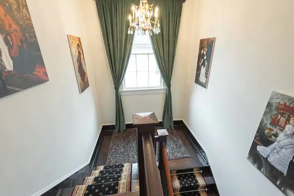 Un couloir orné d’un lustre, de rideaux verts et d’œuvres d’art accrochées aux murs.