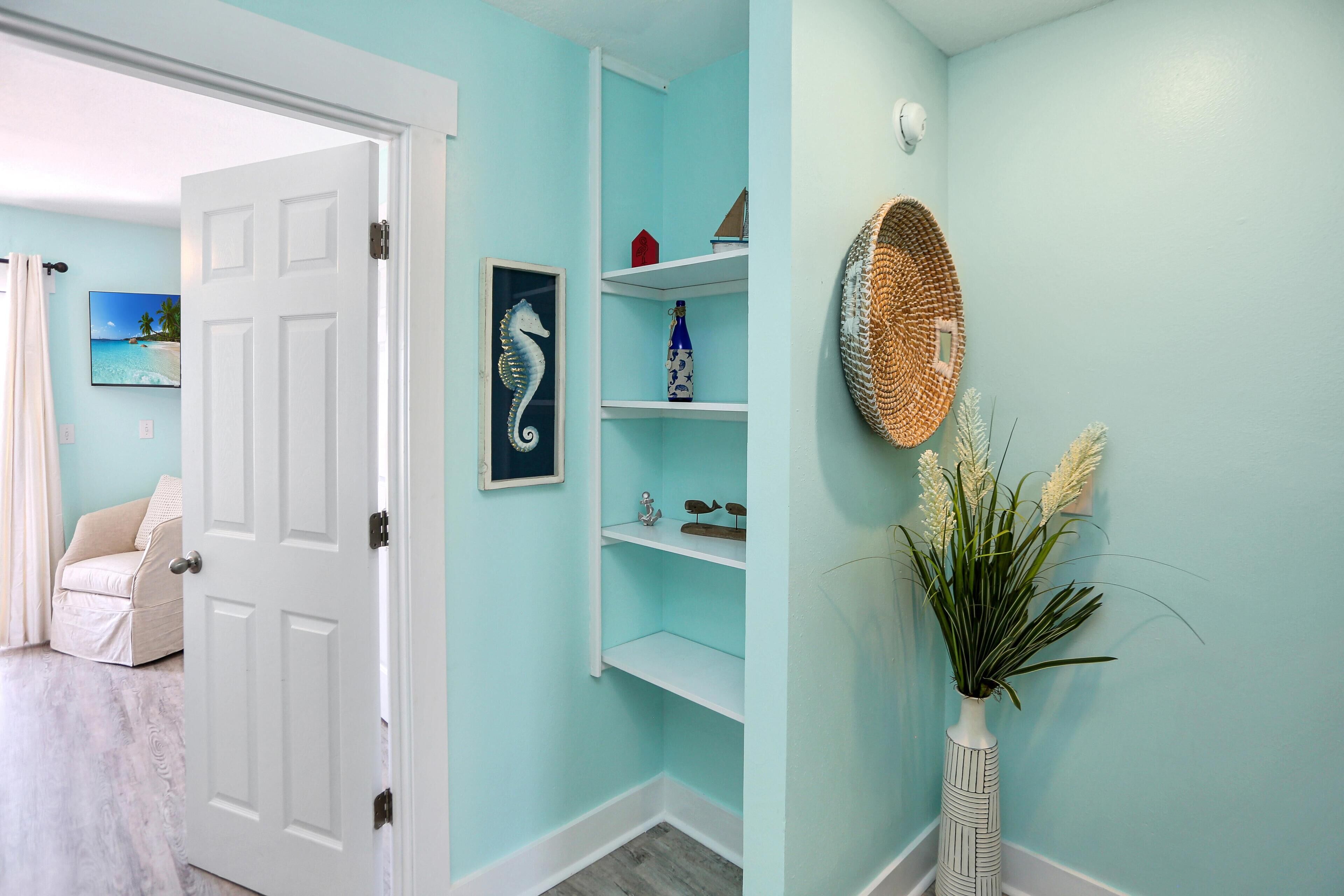 A hallway with light blue walls, white door, and shelves with decorative items.