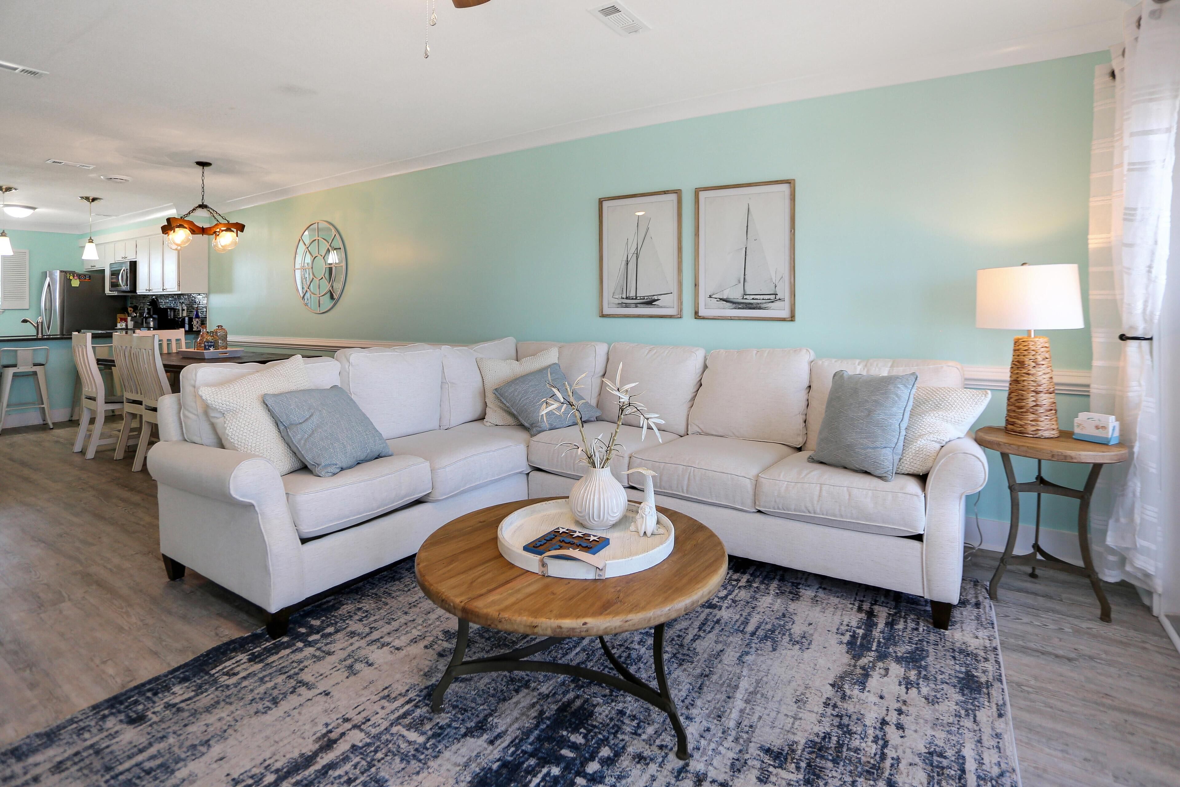 A living room with a white sectional sofa, a round coffee table, and a blue patterned rug.