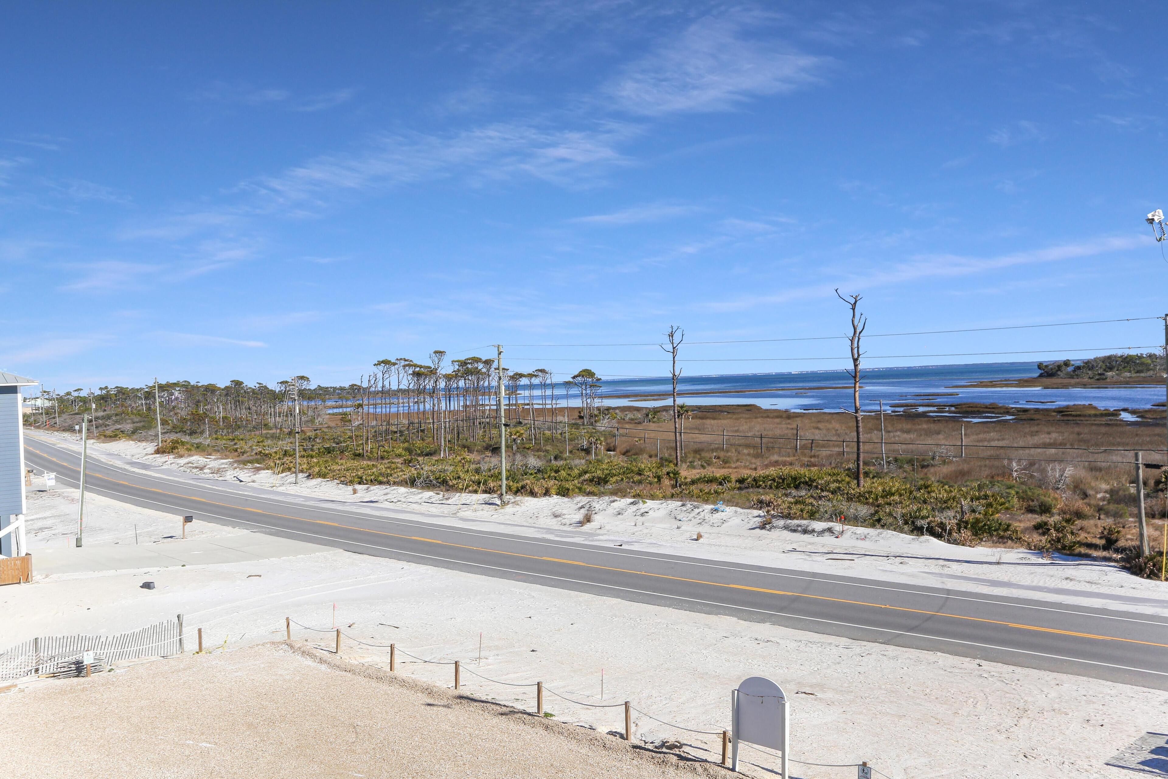Una carretera costera con cielo despejado, playa arenosa y vegetación escasa.