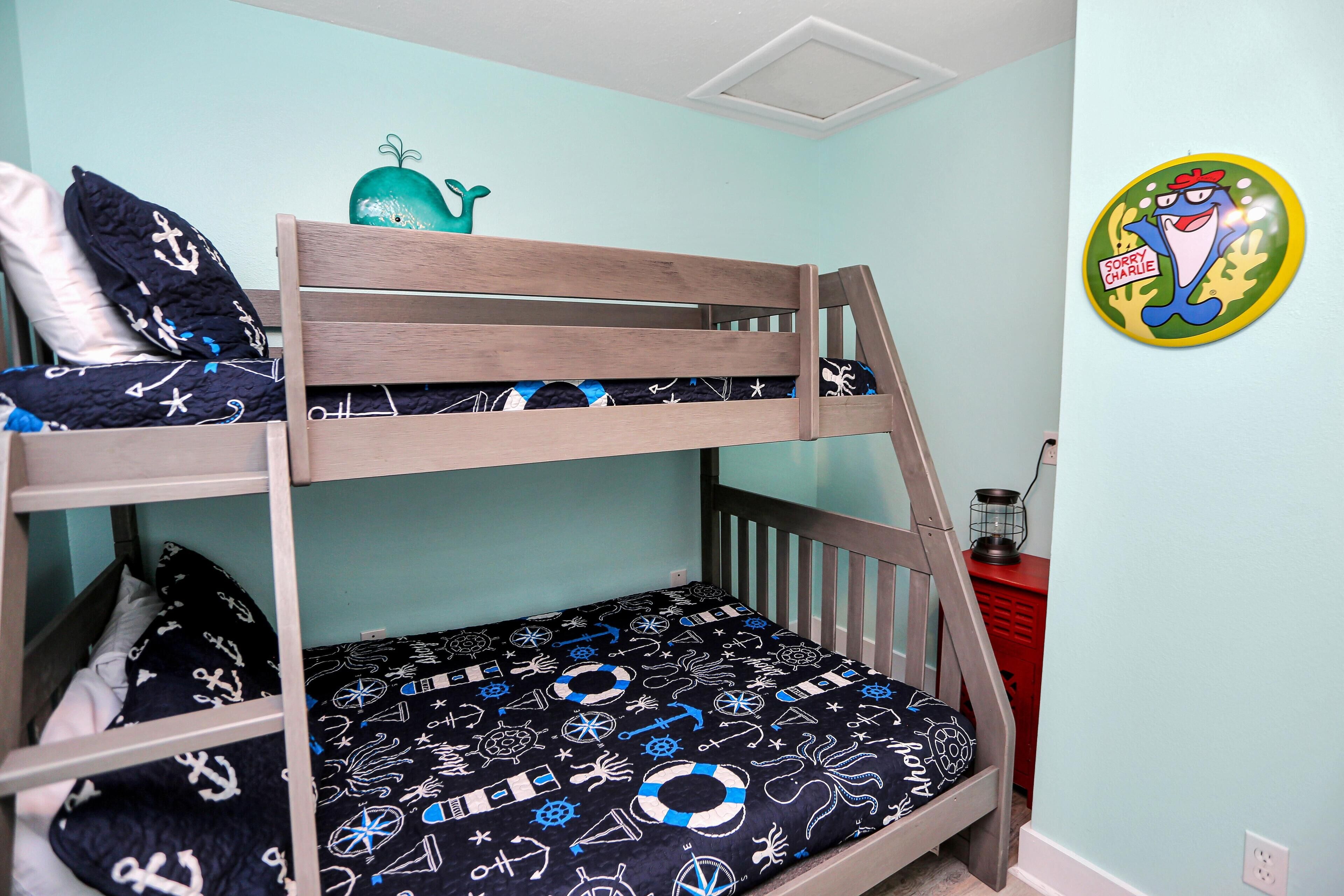 Una cama litera con ropa de cama temática náutica, un aparador rojo y una decoración de pared.