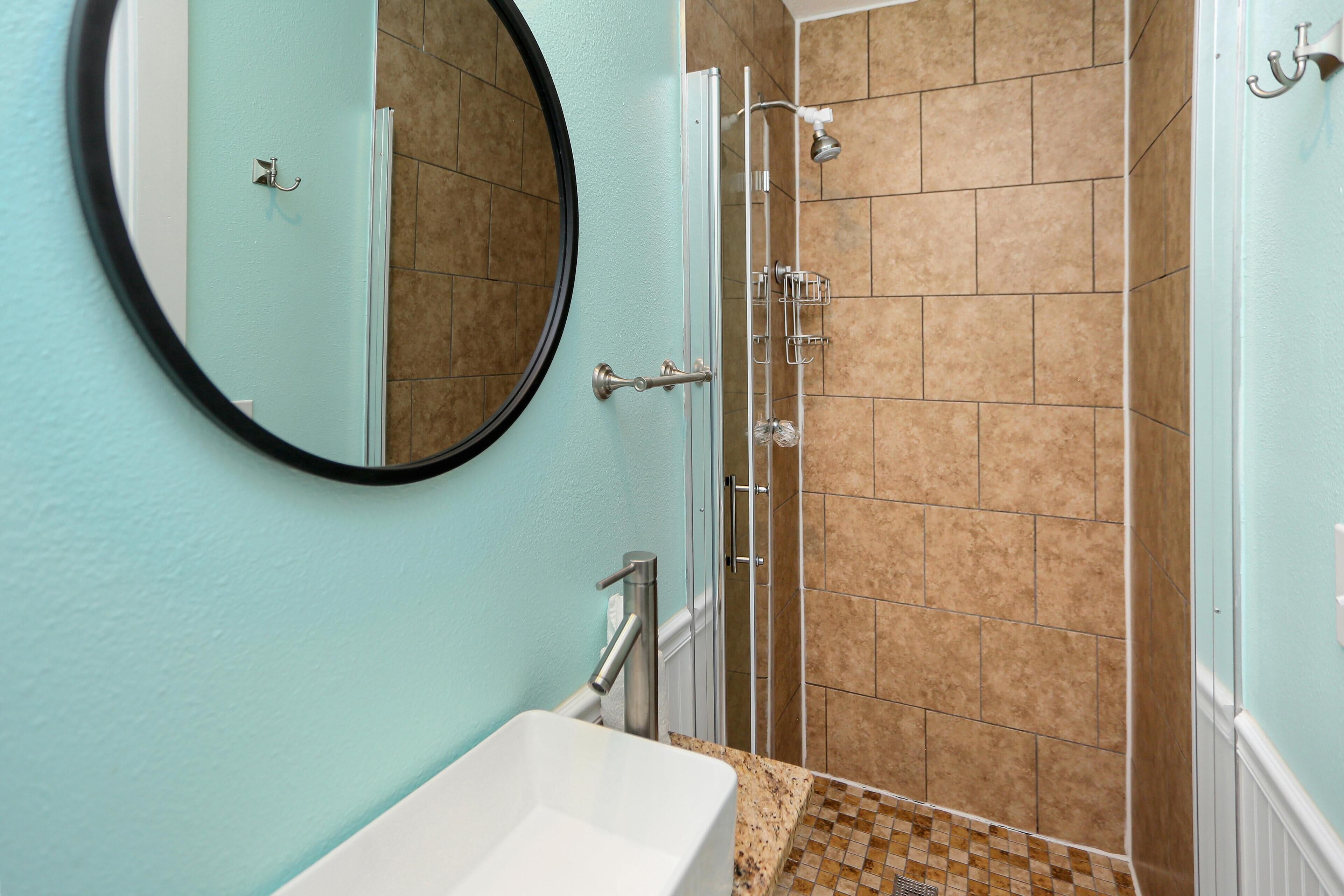 A bathroom with a sink, mirror, and shower.