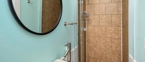 A bathroom with a sink, mirror, and shower.