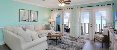 A living room with a white sofa, a round coffee table, and a view of the ocean through large sliding glass doors.