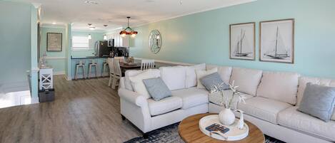 Un salon spacieux avec un canapé blanc, une table basse en bois et un tapis à motifs bleus.