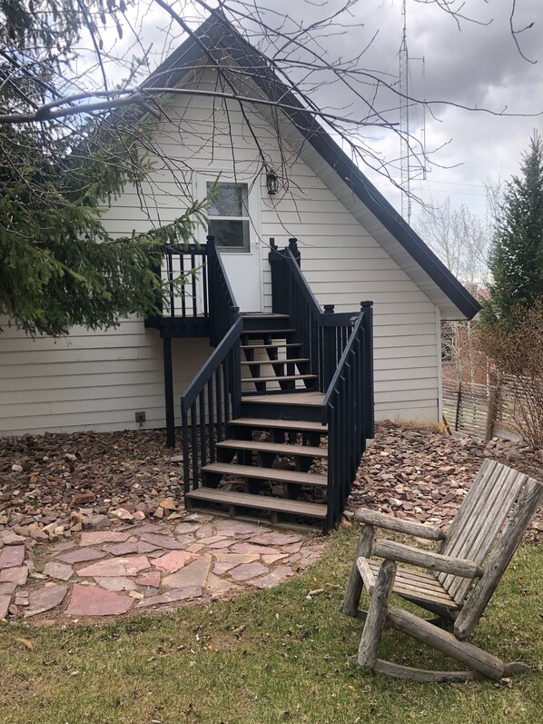 Ein Haus mit einem von Pflastersteinen ausgelegten Vorgarten, einem hölzernen Schaukelstuhl und einer Treppe, die zu einer Veranda führt.