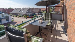 Een balkon met een tafel, stoelen en een parasol.