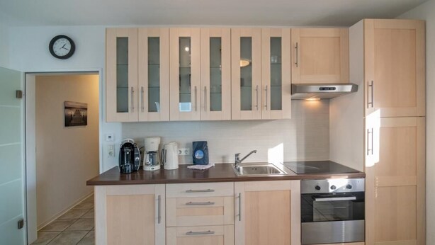 Een moderne keuken met lichte houten kastjes, een roestvrijstalen spoelbak, een inbouwoven en een koffiezetapparaat.