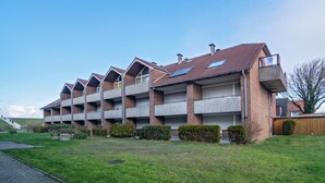 Een meerlaags woongebouw met een bakstenen gevel, meerdere balkons en een schuin dak met zonnepanelen.