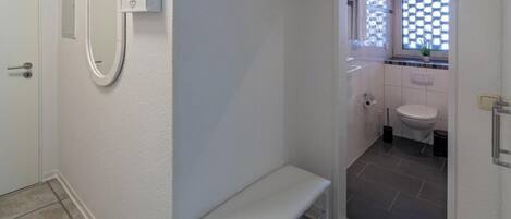 A bathroom with a white bench, a mirror, a window with a checkered pattern, and a toilet.