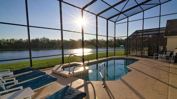 A pool area with a view of a lake, surrounded by a glass enclosure, and equipped with lounge chairs.