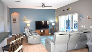 A living room with a flat-screen TV, leather recliners, a wooden entertainment unit, and a large window with a view of the outdoors.