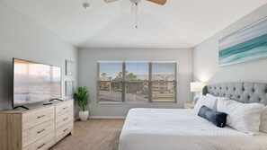 A bedroom with a large bed, a TV, a dresser, a window with blinds, and a ceiling fan. - Luxury Pool Villa, sleeps 14, 5 mins to Disney, Games Room, gated resort (Kissimmee)