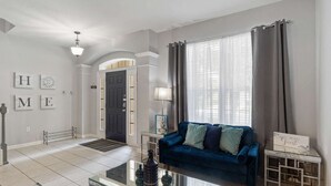 Ein Wohnzimmer mit einem blauen Sofa, einem Glastisch und einer Lampe. Eine Tür ist mit einem Schild versehen, und die Wände sind mit Buchstaben dekoriert.