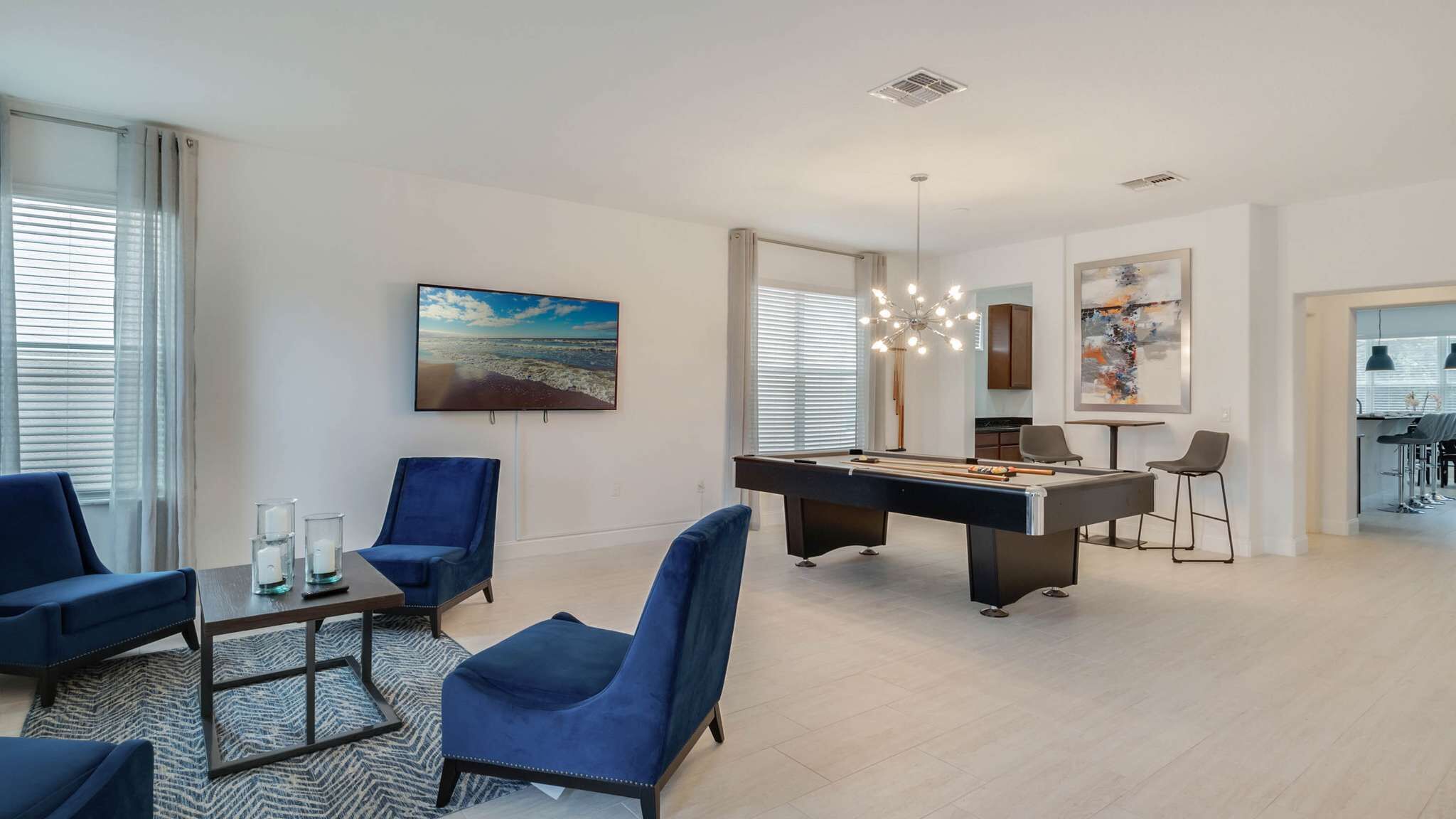 A modern living room with a pool table, blue chairs, and artwork on the walls.