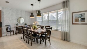 Un coin repas avec une table en bois dressée pour six personnes, entourée de chaises, d’un miroir et d’une plante en pot.
