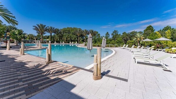 A pool area with lounge chairs and umbrellas, surrounded by palm trees and a clear sky.