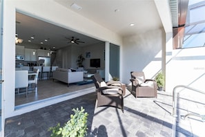 Relax in this open-plan living space with a patio area, featuring a dining table, wicker seating, and a fully equipped kitchen.