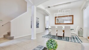 A spacious living area with a staircase, a dining table with chairs, and a large mirror.
