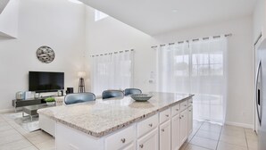 A modern kitchen with a large island, white cabinetry, and a flat-screen TV mounted above the counter.