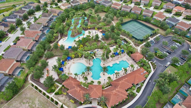 An aerial view of a residential area with a large swimming pool, tennis courts, and a parking lot.