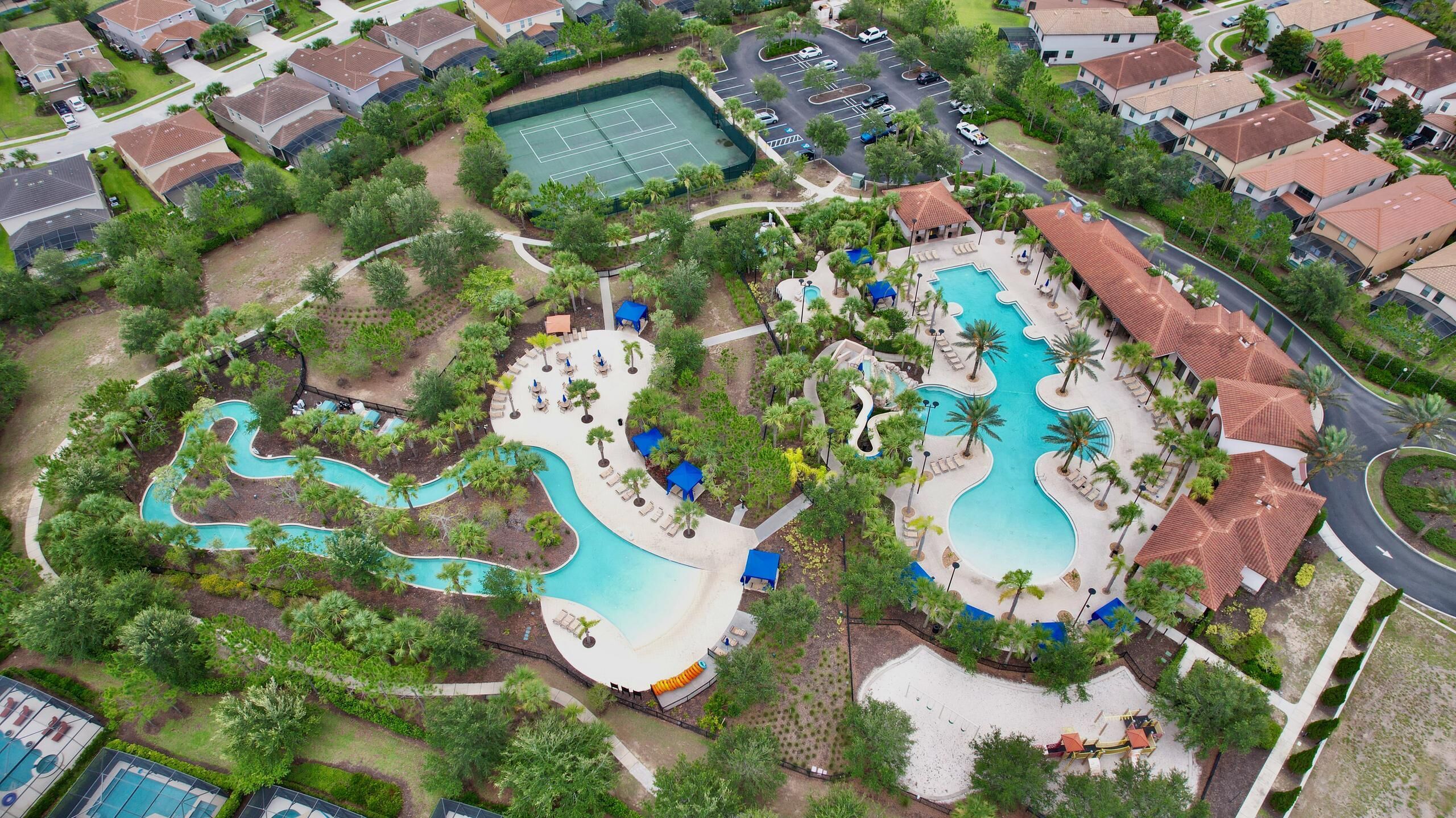 An aerial view of a resort with multiple swimming pools, tennis courts, and a landscaped area with palm trees.