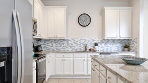 Una cocina con armarios blancos, salpicadero de azulejos y un reloj decorativo en la pared.