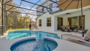 Piscina interior moderna con paredes de vidrio, bañera de hidromasaje y mobiliario exterior.