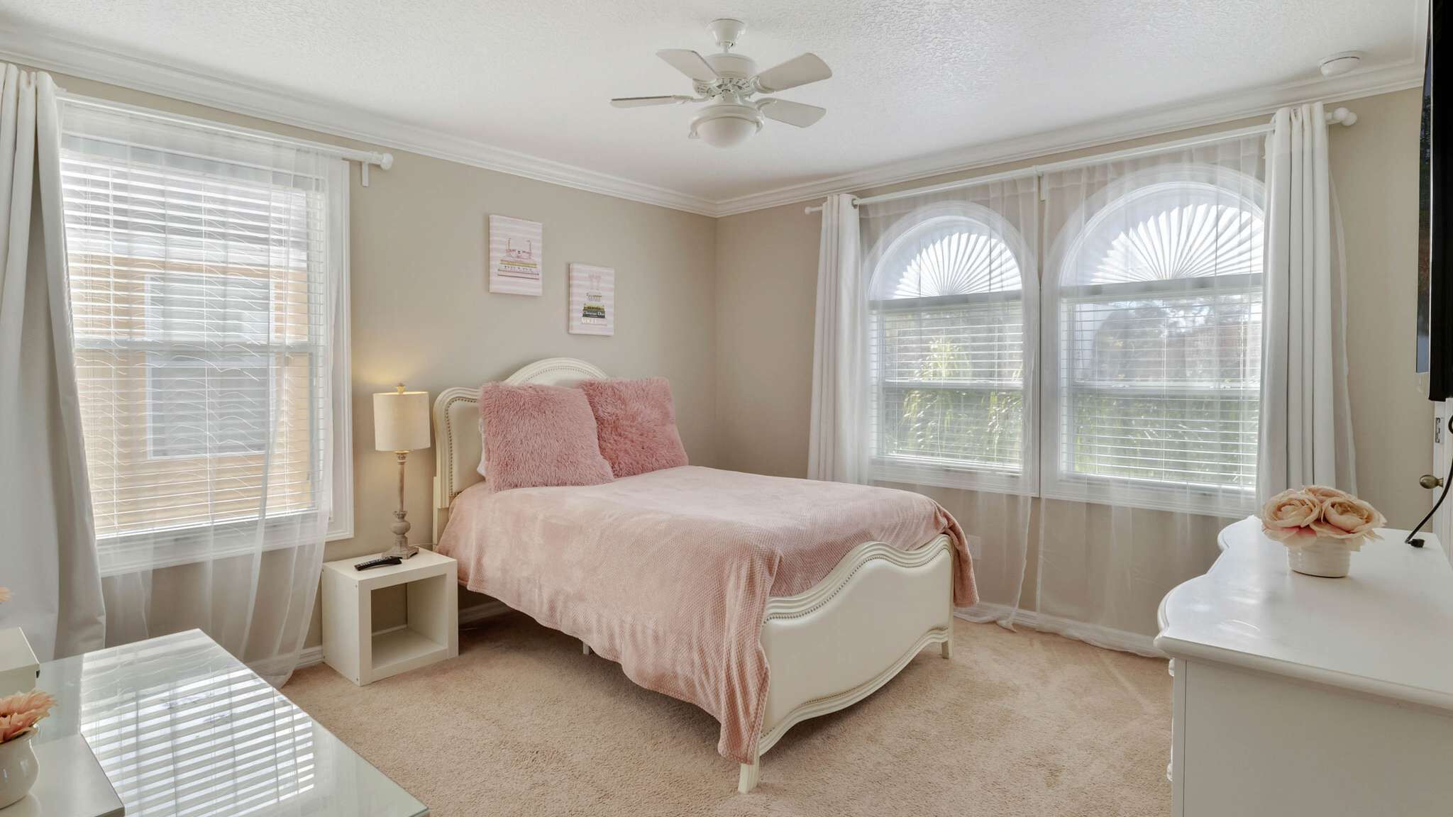 Quarto com cama, mesa de cabeceira, abajur e escrivaninha com um vaso de flores.