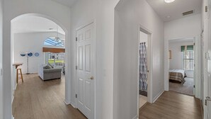 Un pasillo con paredes blancas y suelo de madera, que conduce a una sala de estar con sofá y una mesa de comedor.