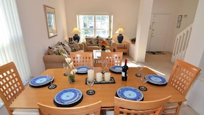 A dining room with a wooden table set for six, featuring blue and white patterned plates, candles, and a bottle of wine. - Family pool home on gated community, private pool & jacuzzi, grill, games room. (Kissimmee)