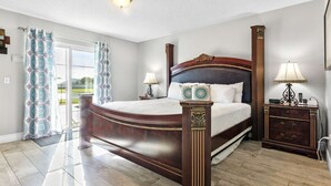 Ein geräumiges Schlafzimmer mit einem großen Bett, zwei Nachttischen, einem Beistelltisch und Blick durch eine Glastür ins Freie.