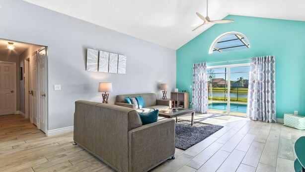 Ein Wohnzimmer mit grauem Sofa, Couchtisch und Lampe. Durch die Glastüren ist ein Pool zu sehen.