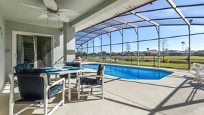 Ein überdachter Poolbereich mit Tisch und Stühlen, einem Deckenventilator und Blick auf eine Wohngegend.