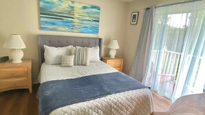 A bedroom with a bed, two nightstands, a painting, and a window with curtains.