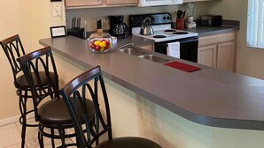 A kitchen with a central island, bar stools, a kettle, and a coffee maker.