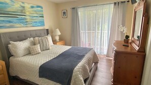 A bedroom with a large bed, a nightstand, a dresser, a painting, and a window with curtains.