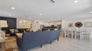 Una sala moderna con un sofá azul, un comedor con sillas blancas y una cocina al fondo.