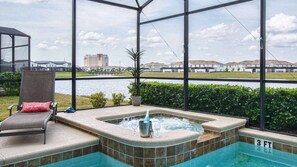 Un espace piscine comprenant un jacuzzi, une chaise longue et une vue sur un lac et des bâtiments.