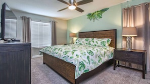 Un dormitorio con cama, escritorio, silla, ventilador de techo y ventana con cortinas.