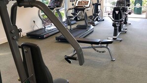 Une salle de sport équipée de divers appareils, notamment des tapis de course, un vélo d’appartement et un banc de musculation.
