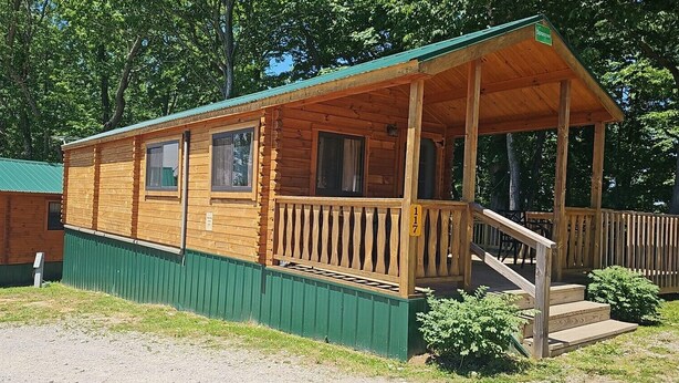 Una cabaña de madera con porche y fachada verde.