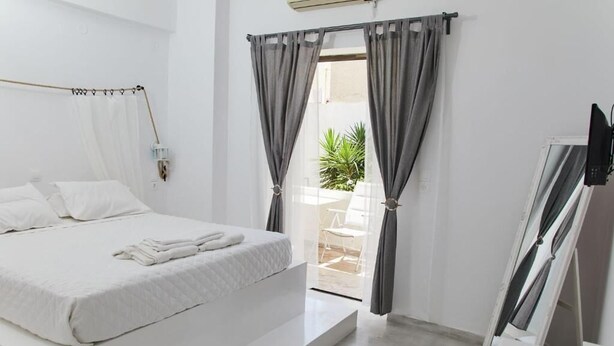 A modern bedroom with a large bed, a small table, and a TV. - Golden Star Praxitelous (Aegina)