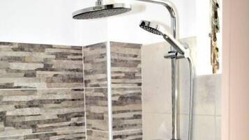 A shower with a rain shower head and handheld showerhead, a vertical glass partition, and a tiled wall with a stone-like pattern.