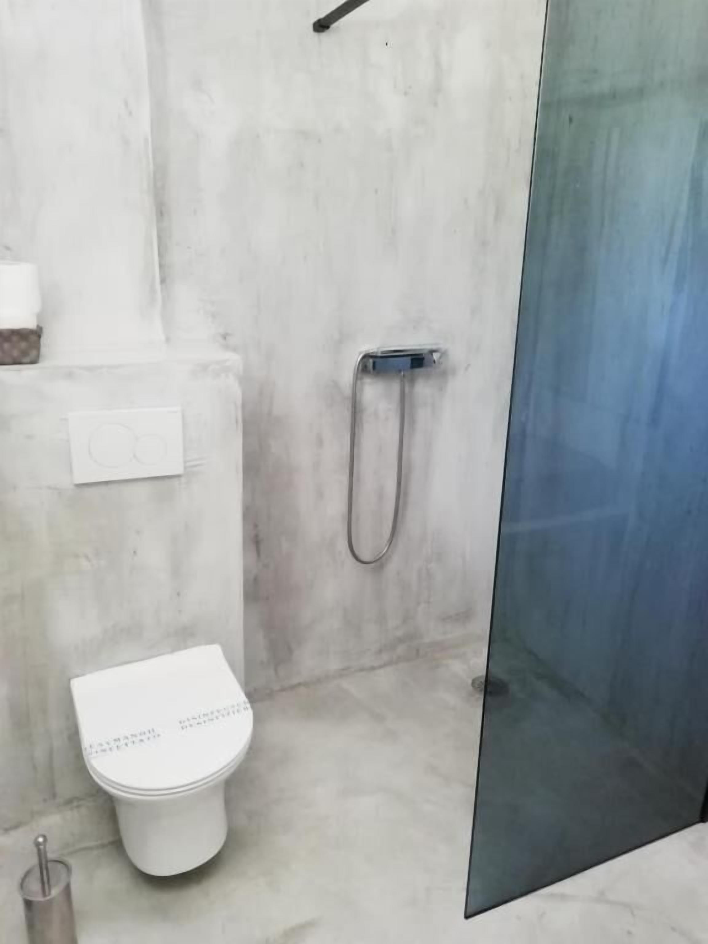 Egy fürdőszoba, amelyben WC, zuhanyzó és üvegfallal elválasztott zuhanyzósarok található.